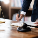 Man in suit with notebook, gavel, and scale of justice on table